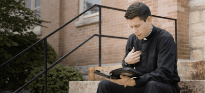 Deacon Jeremy sitting on concrete steps and reading the Bible.